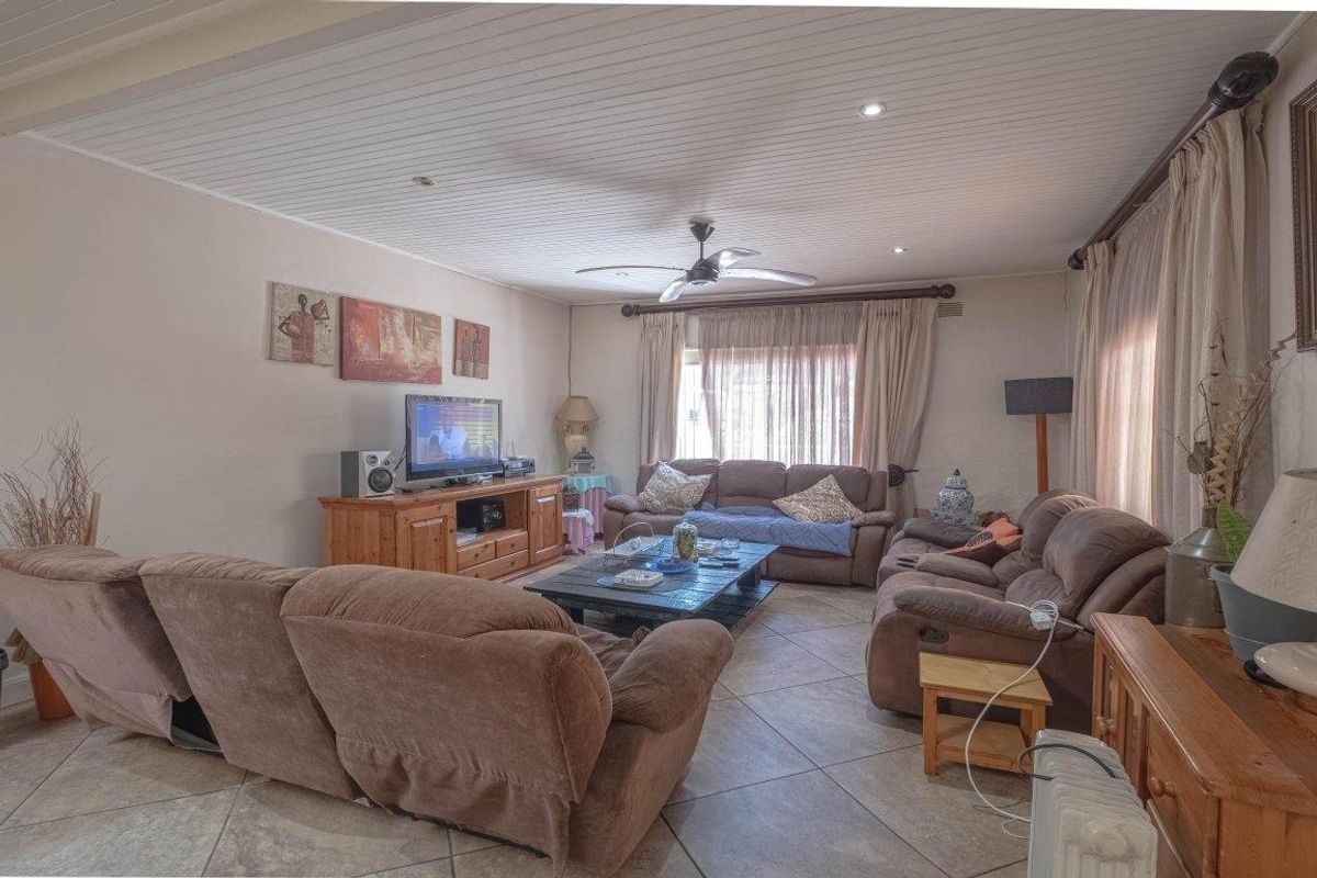 A spacious living room featuring tiled flooring, a tongue and groove ceiling with recessed lighting, and a central ceiling fan.