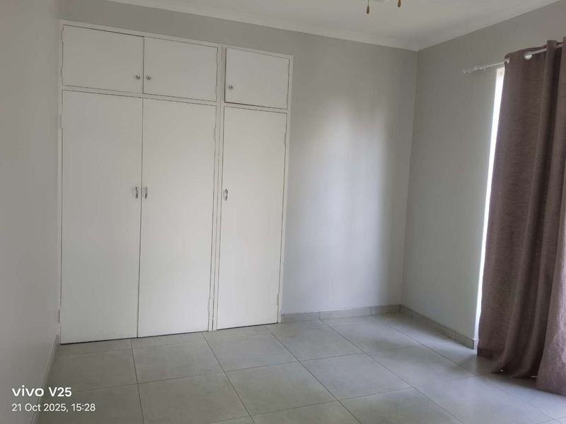 A clean, empty bedroom featuring neutral tiled flooring and ample built-in cupboard storage space.