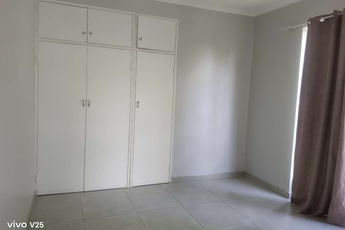 A clean, empty bedroom featuring neutral tiled flooring and ample built-in cupboard storage space.