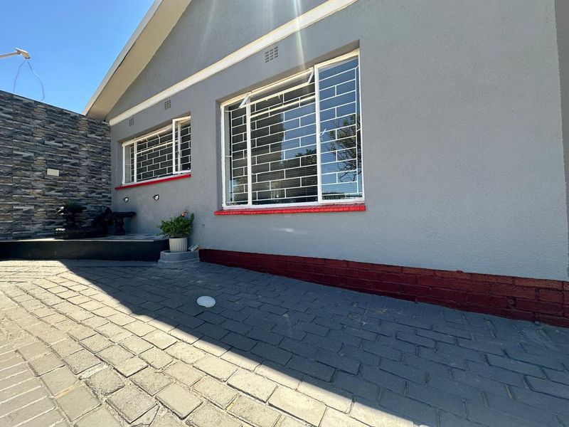 Front exterior view of the house featuring grey painted walls, stone cladding accents, security bars on windows, and a paved driveway area.