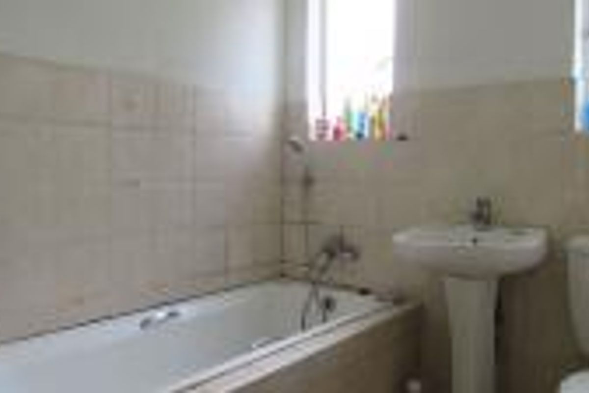 A functional bathroom featuring a standard bathtub, pedestal sink, and toilet with neutral wall tiling and natural light from a window.