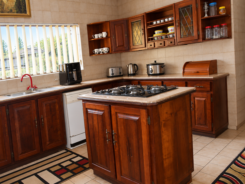A traditional kitchen featuring warm-toned wooden cabinetry, stone countertops, a central island with a built-in gas hob, and tiled finishes throughout.