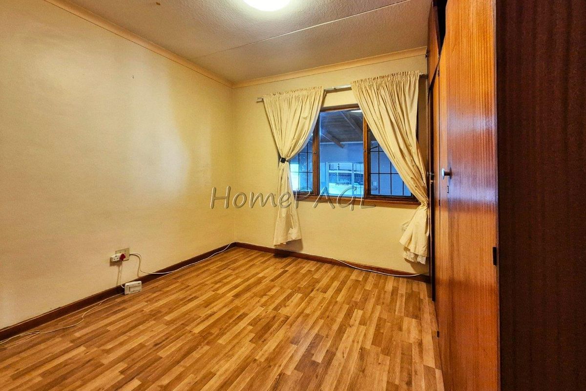 A vacant bedroom featuring laminate flooring, built-in wooden cupboards, and a window with security bars, offering a blank canvas for personalization.