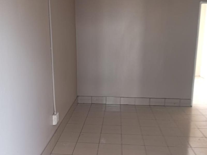 An empty living area featuring neutral ceramic floor tiles and visible surface-mounted electrical conduit along the wall.