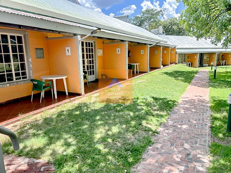 Exterior view of a hotel wing featuring a row of individual guest room entrances with covered patios and a brick pathway through the garden.