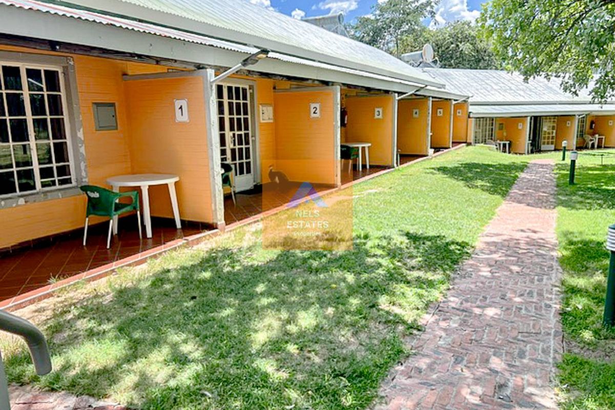 Exterior view of a hotel wing featuring a row of individual guest room entrances with covered patios and a brick pathway through the garden.