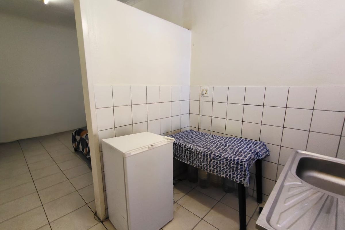 A functional kitchenette area featuring tiled splashbacks, a stainless steel sink, and tiled flooring, providing a practical utility space within the office layout.