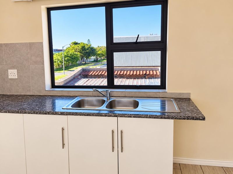 A clean, modern kitchen area featuring a double bowl stainless steel sink, laminate countertops, and white base cabinetry with a tiled splashback.