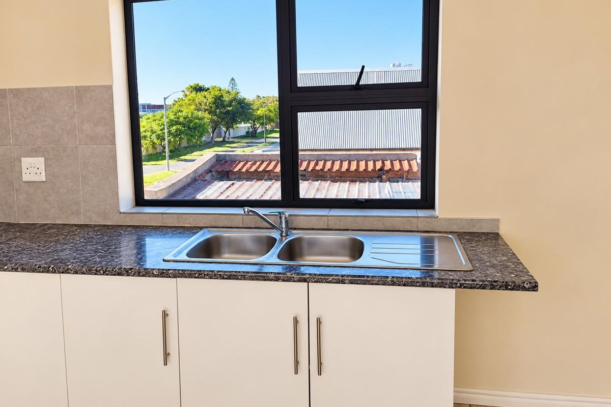 A clean, modern kitchen area featuring a double bowl stainless steel sink, laminate countertops, and white base cabinetry with a tiled splashback.