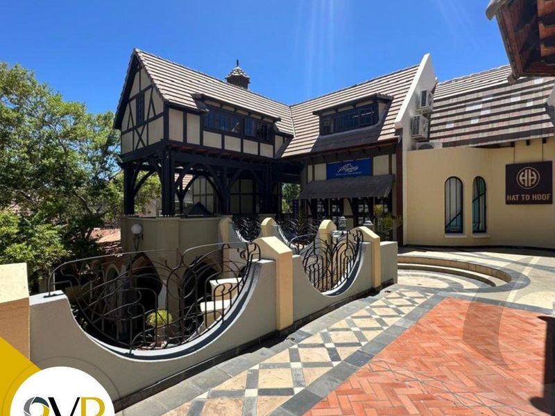 A well-maintained office building exterior featuring distinctive timber-framed architecture, decorative wrought iron railings, and patterned brick paving in a sunny courtyard setting.