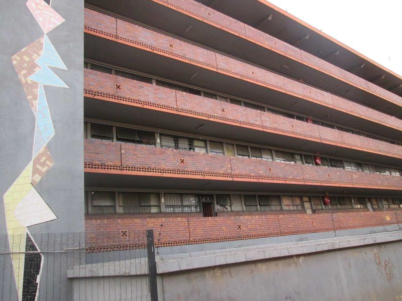 Exterior view of a multi-story apartment building featuring a brick facade, integrated balconies, and a decorative mosaic feature wall.