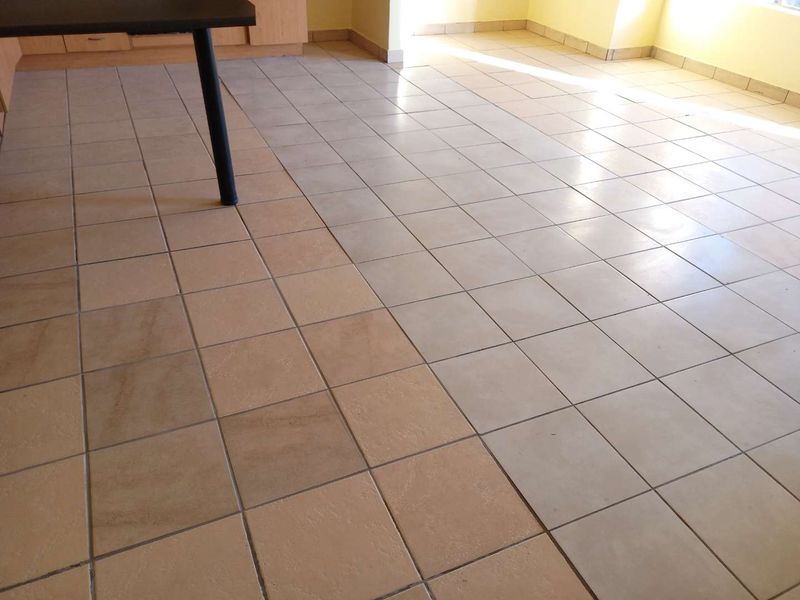 An empty open-plan living area featuring mismatched ceramic floor tiles and yellow wall paint.
