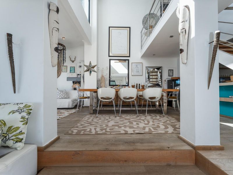 Spacious open-plan living and dining area featuring double volume ceilings, timber flooring, and a mezzanine level with a modern staircase.
