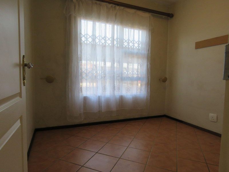 An empty bedroom featuring tiled flooring and a window with a curtain rod, presenting a blank canvas for potential interior design updates.