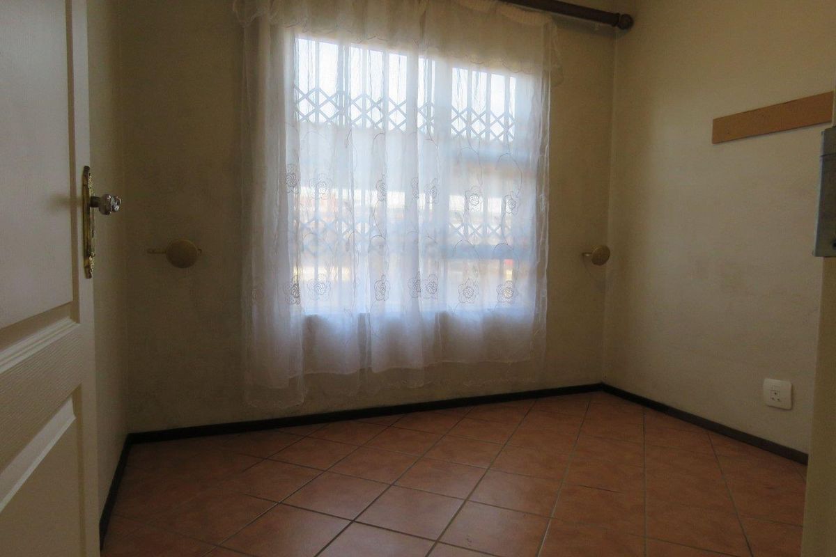 An empty bedroom featuring tiled flooring and a window with a curtain rod, presenting a blank canvas for potential interior design updates.