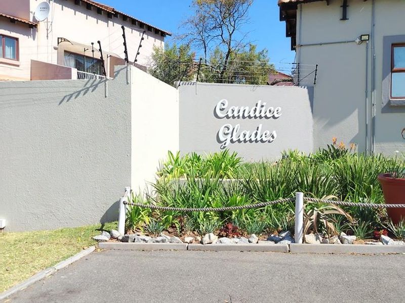 Front entrance view of Candice Glades townhouse complex featuring a boundary wall with electric fencing and paved driveway access.
