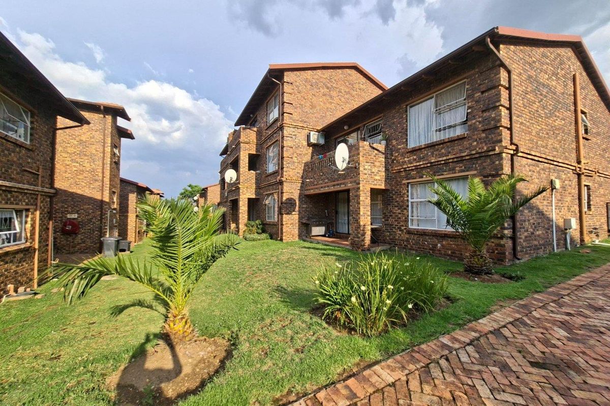 Exterior view of a multi-story brick apartment complex featuring landscaped garden areas, paved walkways, and private balconies.