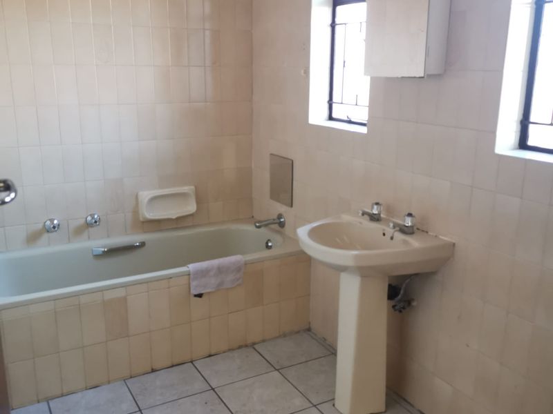 A dated bathroom featuring a pedestal basin, built-in bathtub, and full-height wall tiling, offering a blank canvas for modern renovation.