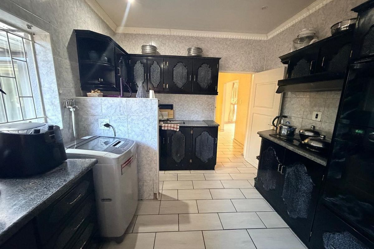A functional kitchen featuring dark cabinetry, tiled walls, and floor tiles, with integrated laundry space and direct access to the hallway.