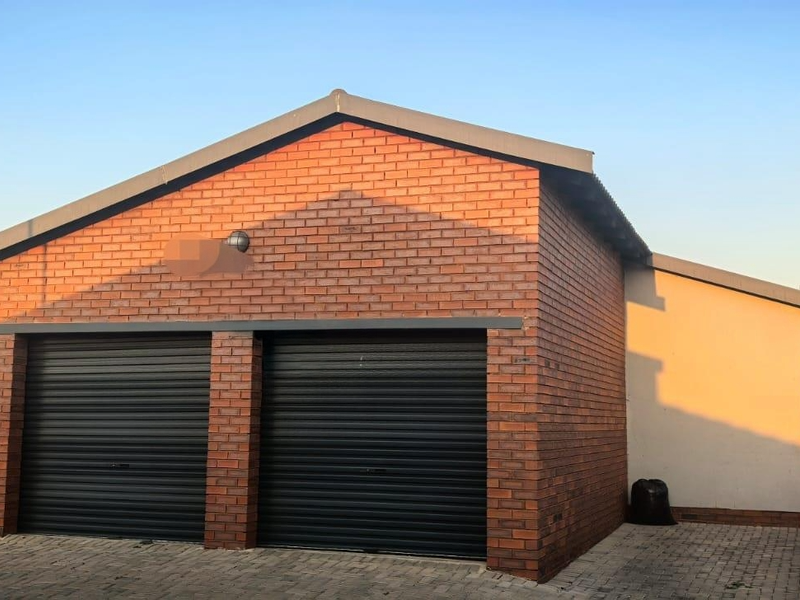 A double garage featuring a face brick exterior, black roller doors, and a paved driveway area.