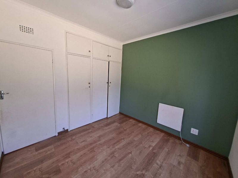 An empty bedroom featuring laminate flooring, built-in cupboards, and a wall-mounted heater, ready for personalization.