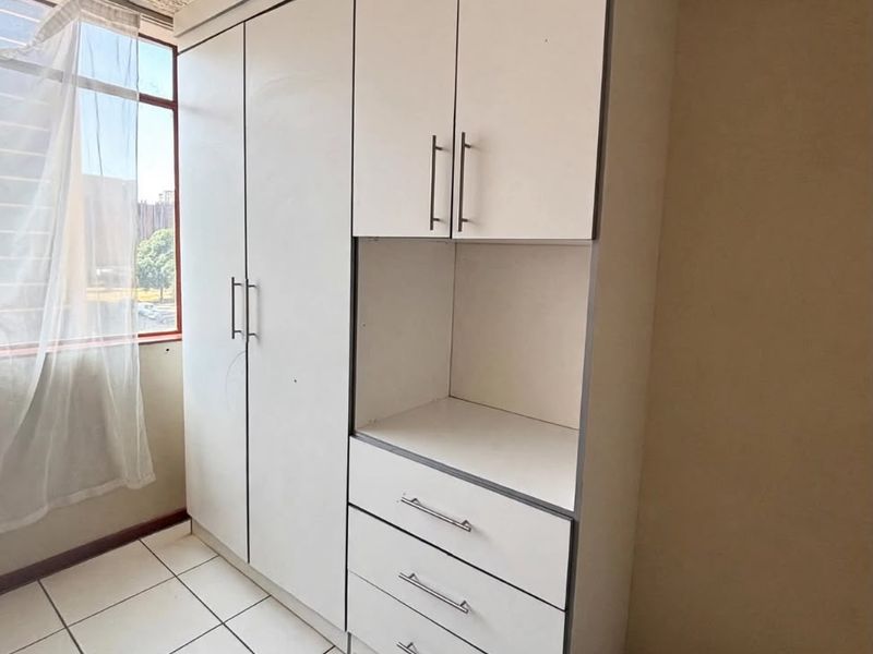A bedroom featuring a built-in white wardrobe with integrated drawers and shelving, complemented by ceramic floor tiles and a textured ceiling.