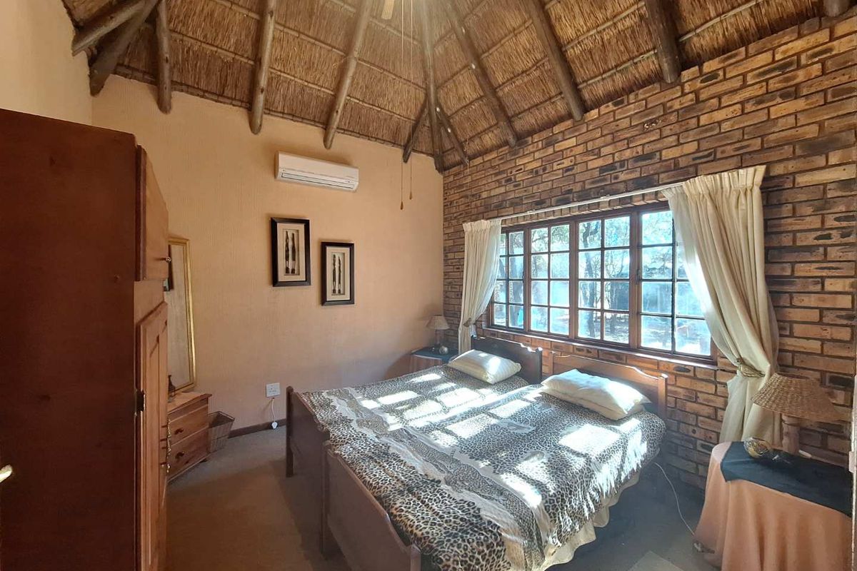 A rustic bedroom featuring a high vaulted thatch ceiling, exposed brick feature wall, and a split-system air conditioning unit.