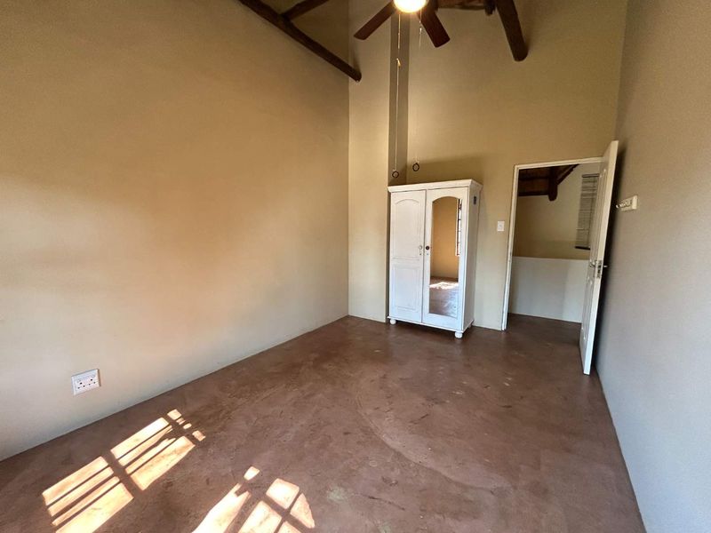 A spacious bedroom featuring high ceilings with exposed timber beams, a ceiling fan, and durable concrete flooring, offering a blank canvas for personalization.
