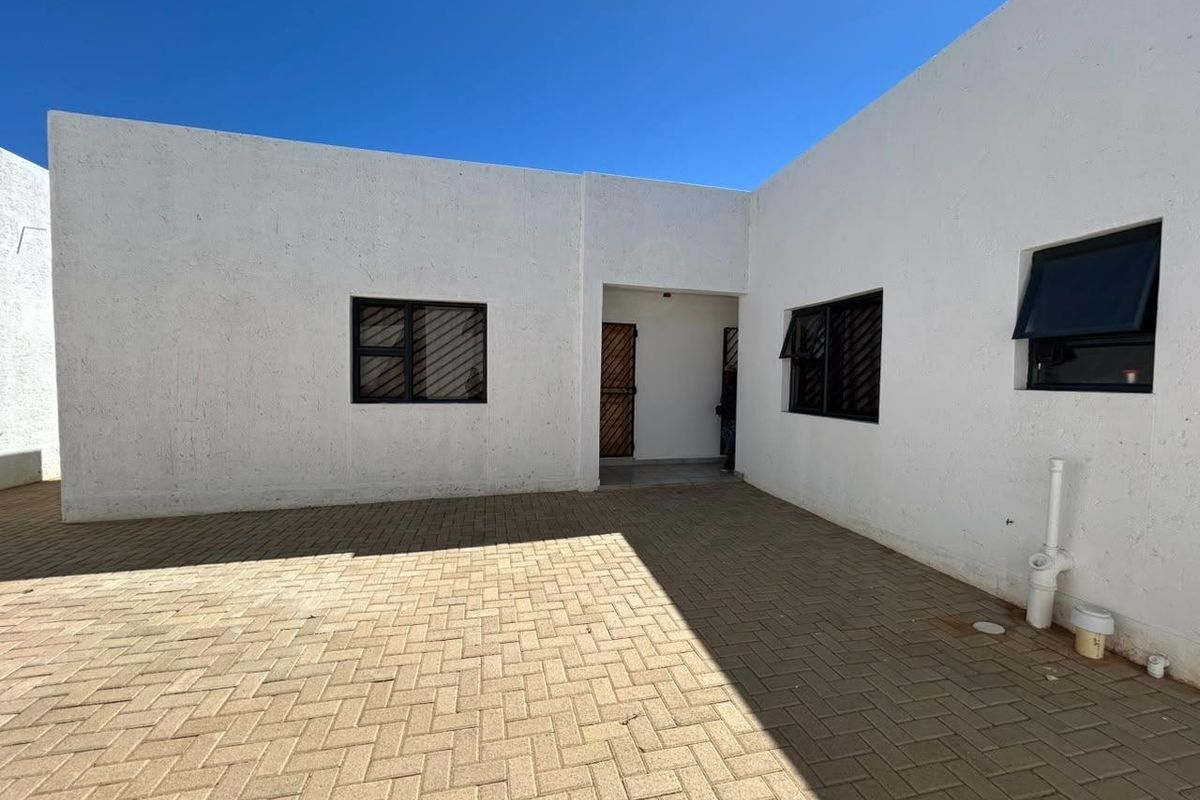 A clean, paved rear courtyard area featuring white exterior walls, security-fitted windows, and a secure entrance gate.