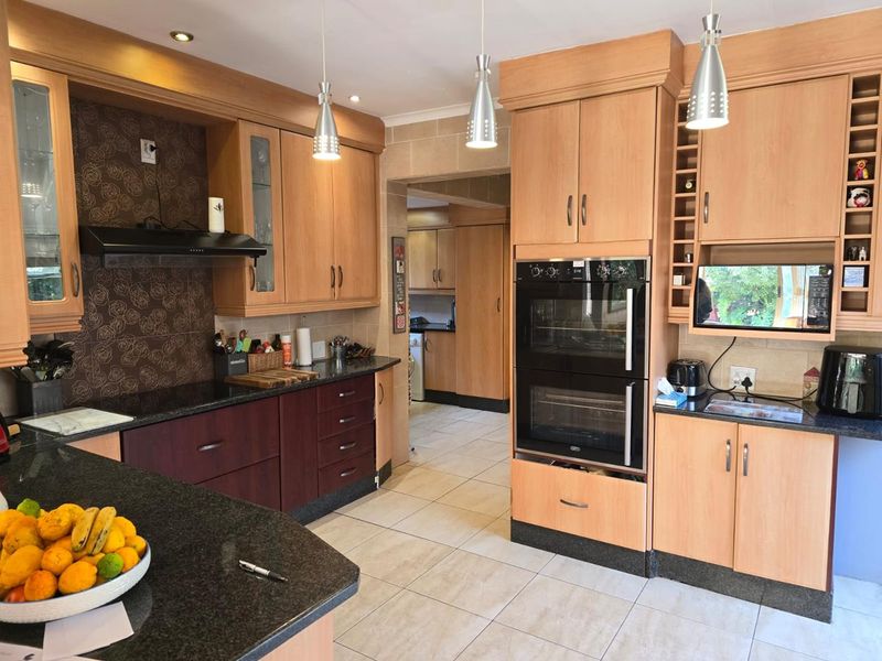 A well-maintained kitchen featuring granite countertops, built-in double oven, extractor fan, and ample cabinetry, with an adjoining scullery area.