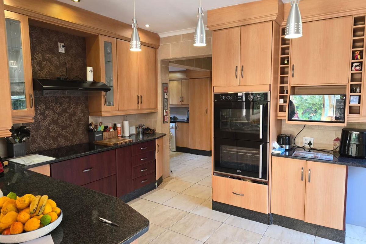 A well-maintained kitchen featuring granite countertops, built-in double oven, extractor fan, and ample cabinetry, with an adjoining scullery area.