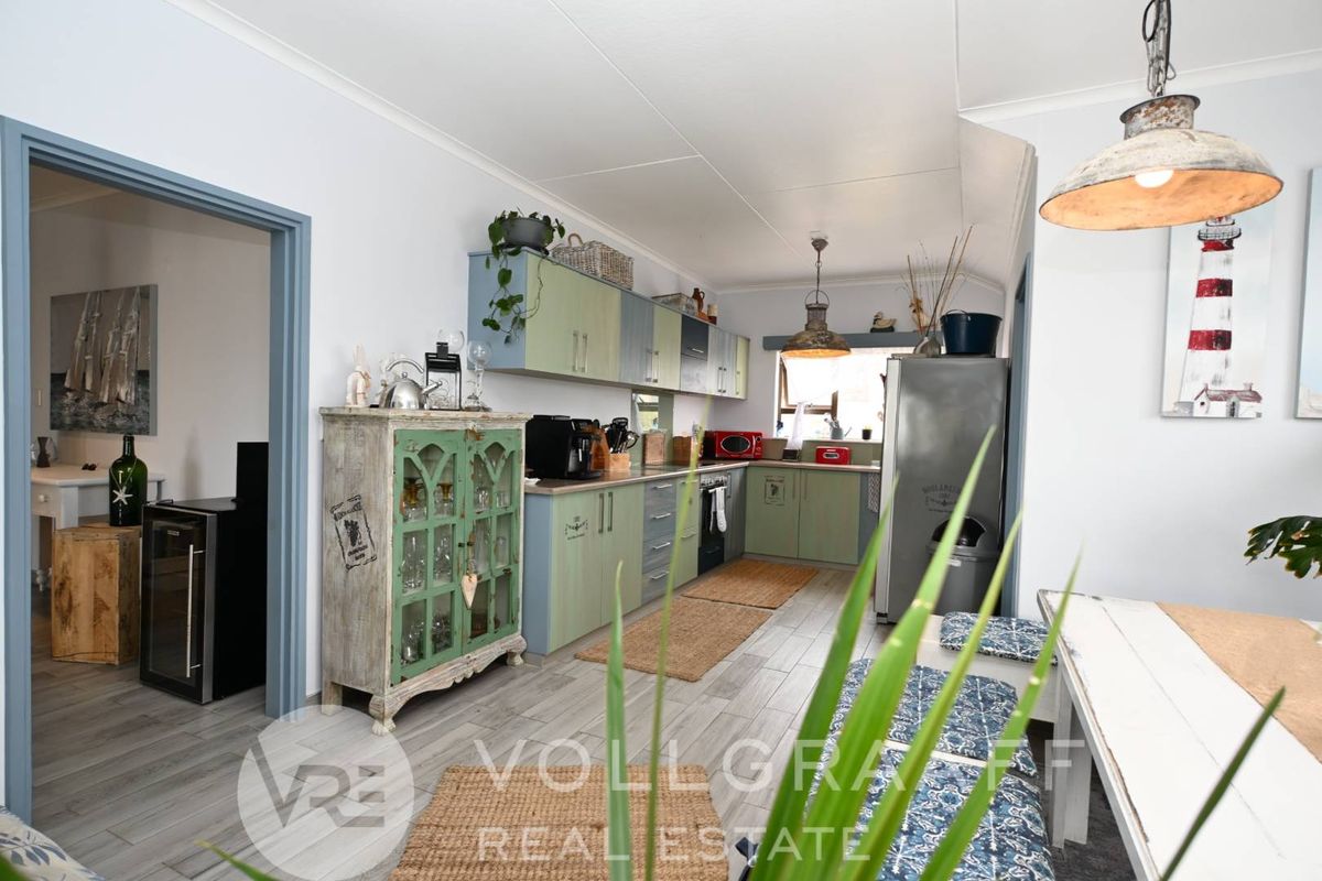 A functional kitchen featuring light green cabinetry, wood-look tile flooring, and integrated lighting, offering a practical layout with adjacent dining space.