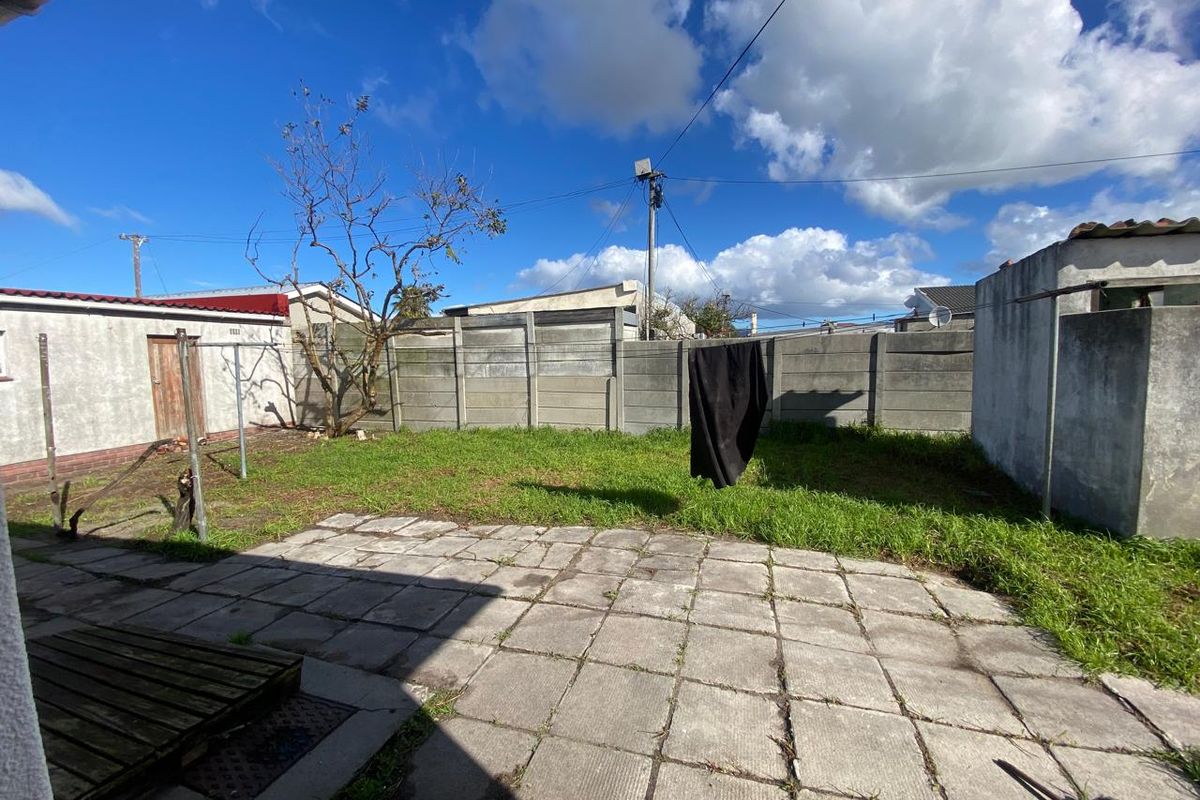A rear garden area featuring a paved patio, grass lawn, and concrete boundary walling, offering potential for landscaping and outdoor improvement.