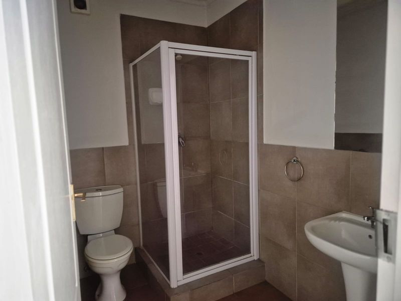 A functional bathroom featuring a shower enclosure, pedestal basin, and toilet with neutral wall and floor tiling.