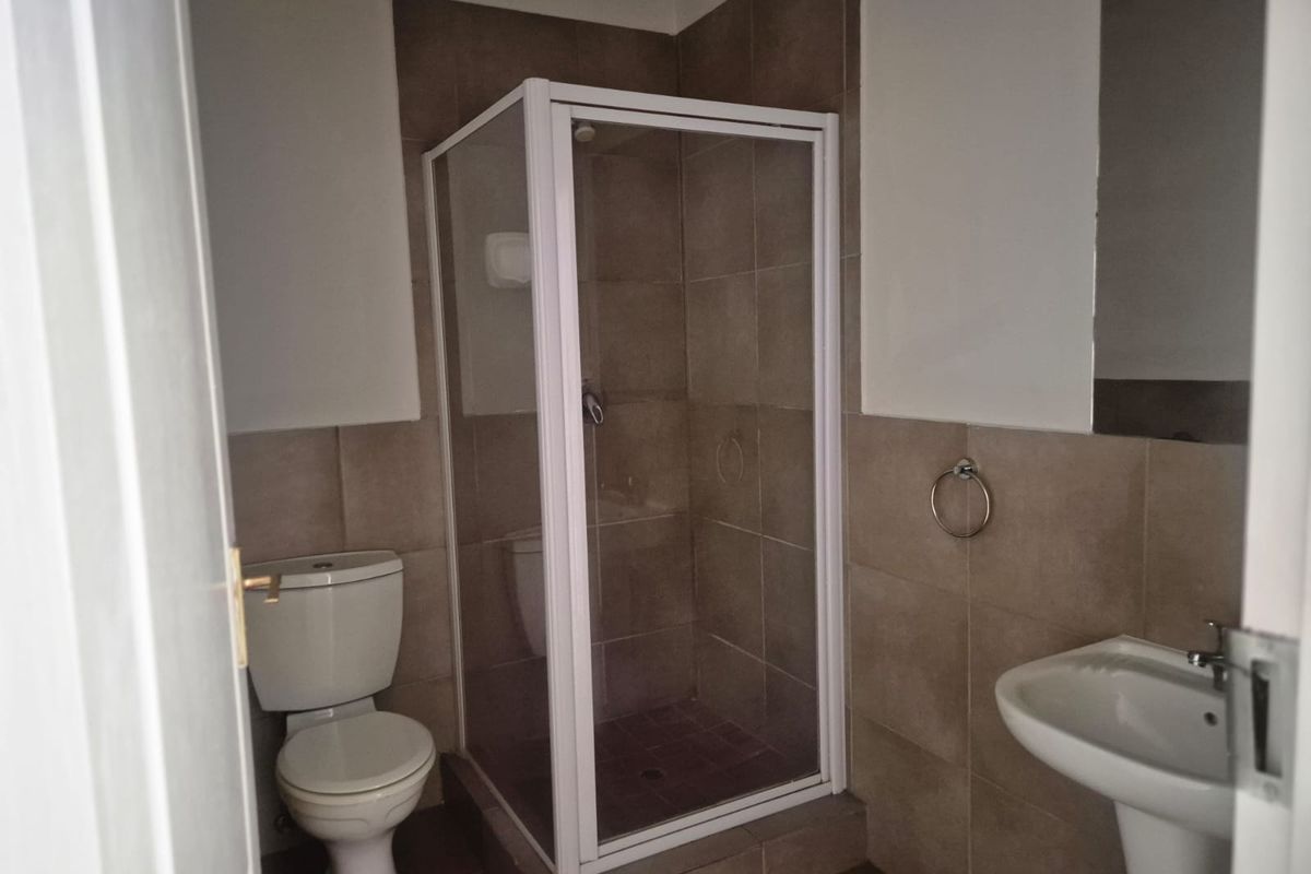 A functional bathroom featuring a shower enclosure, pedestal basin, and toilet with neutral wall and floor tiling.
