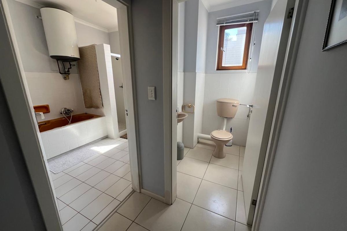 A view into a dated bathroom suite featuring a separate bathtub, shower area, and toilet with older style sanitary fixtures.