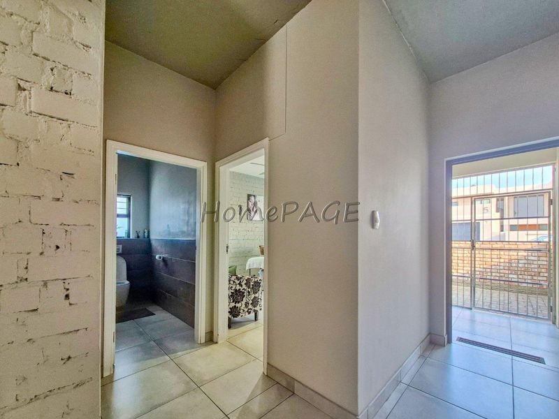 A bright hallway featuring tiled flooring and exposed brick accents, providing access to adjacent rooms and an exterior security gate.