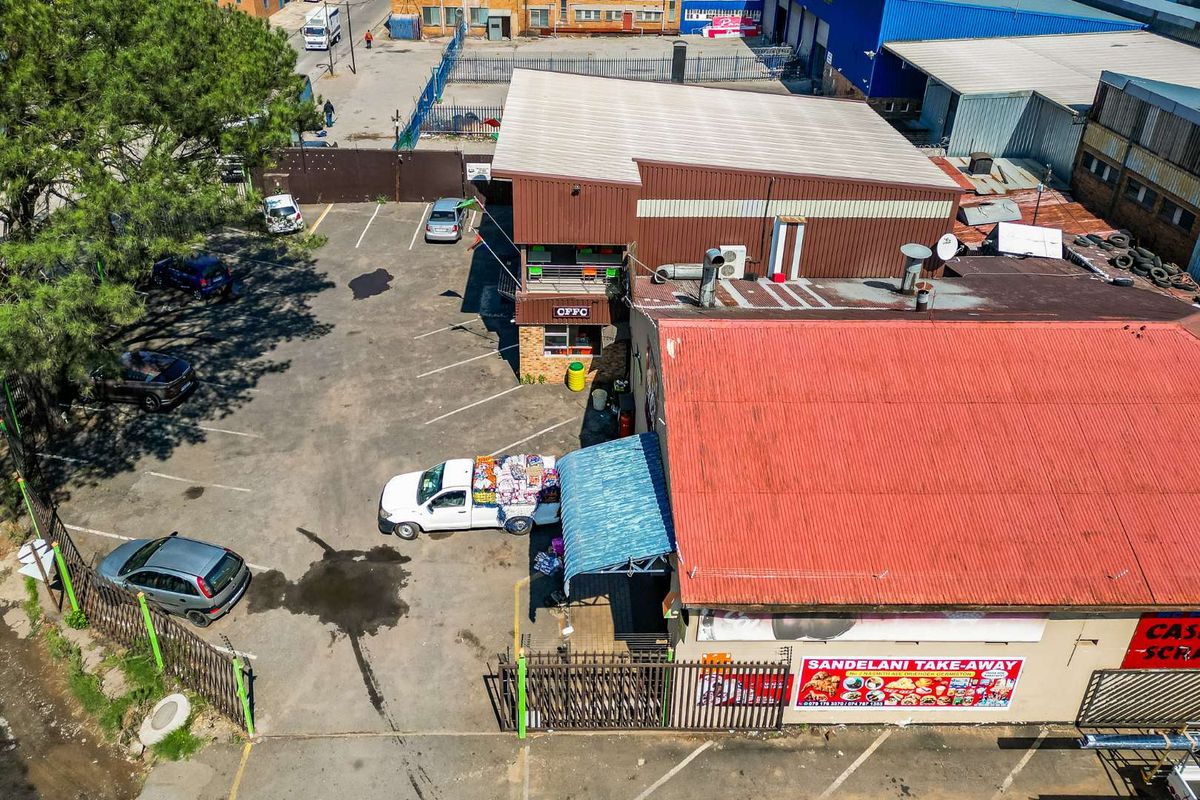 Aerial view of a commercial property featuring a multi-level building, paved parking area, and corrugated metal roofing.