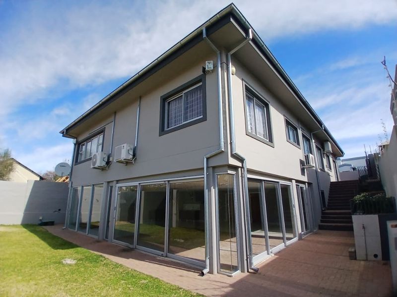 Rear view of a two-story house featuring extensive sliding glass doors, paved patio area, external staircase, and well-maintained exterior walls.