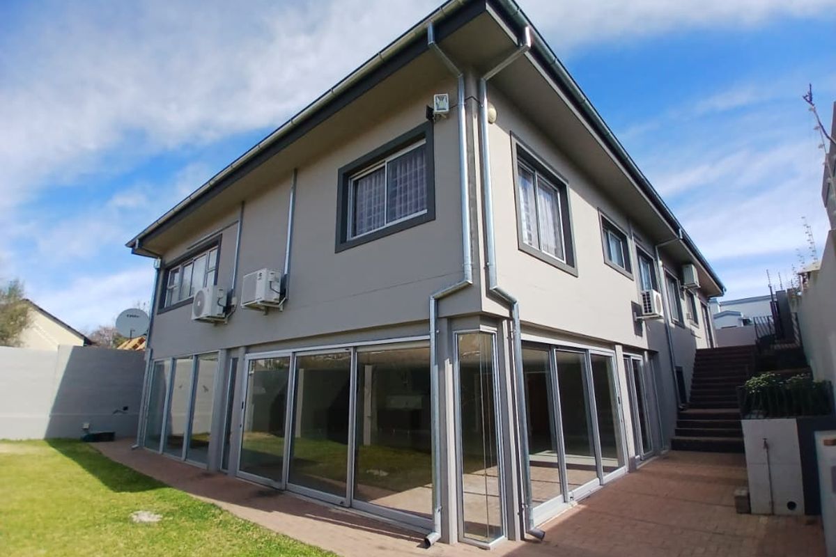 Rear view of a two-story house featuring extensive sliding glass doors, paved patio area, external staircase, and well-maintained exterior walls.
