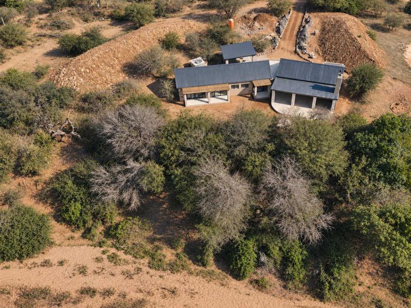 Aerial view of a modern house with a metal roof, featuring a covered patio and surrounding natural bushveld landscape.