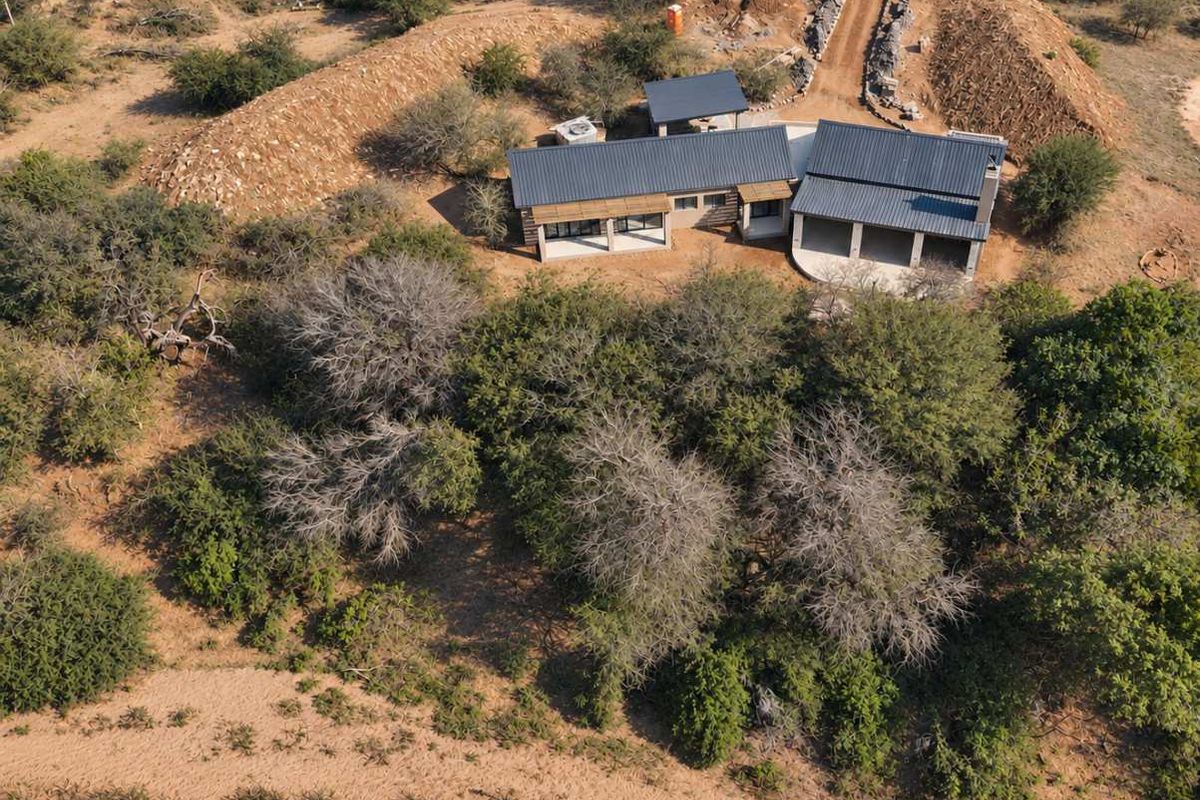 Aerial view of a modern house with a metal roof, featuring a covered patio and surrounding natural bushveld landscape.