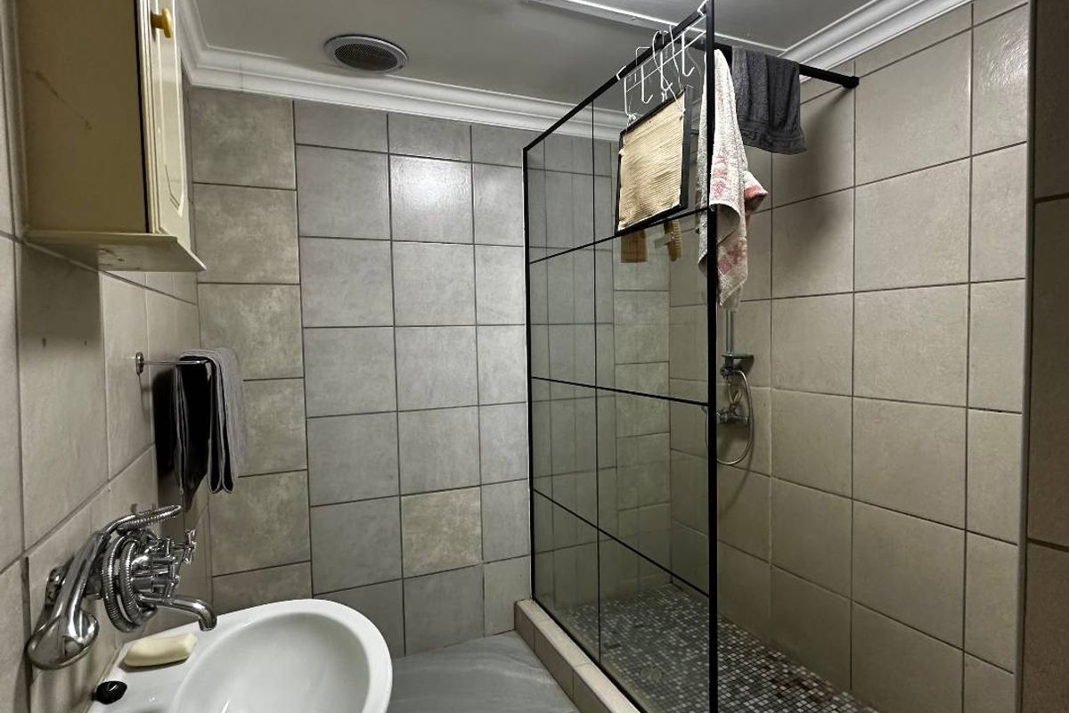 A functional bathroom featuring a walk-in shower with a black-framed glass screen, tiled walls, and a pedestal basin.