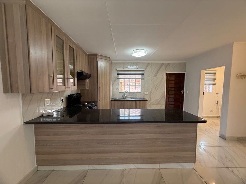 Modern kitchen featuring wood-finish cabinetry, granite countertops, marble-look wall tiles, and tiled flooring, offering a clean and functional workspace.