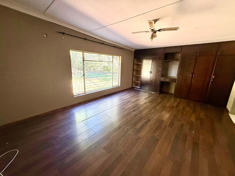 Spacious bedroom featuring dark wood-look laminate flooring, extensive built-in cabinetry, a ceiling fan, and large windows with security bars.