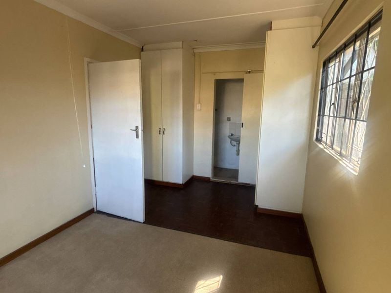 An empty bedroom featuring built-in cupboards, security bars on the window, and a combination of carpet and vinyl flooring.