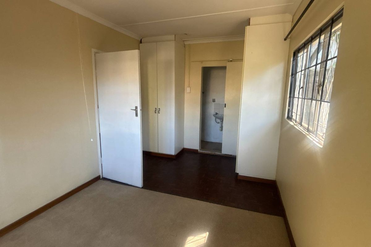 An empty bedroom featuring built-in cupboards, security bars on the window, and a combination of carpet and vinyl flooring.