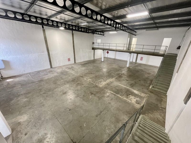Spacious industrial warehouse unit featuring high ceilings with exposed steel trusses, a mezzanine level, concrete flooring, and internal staircase access.