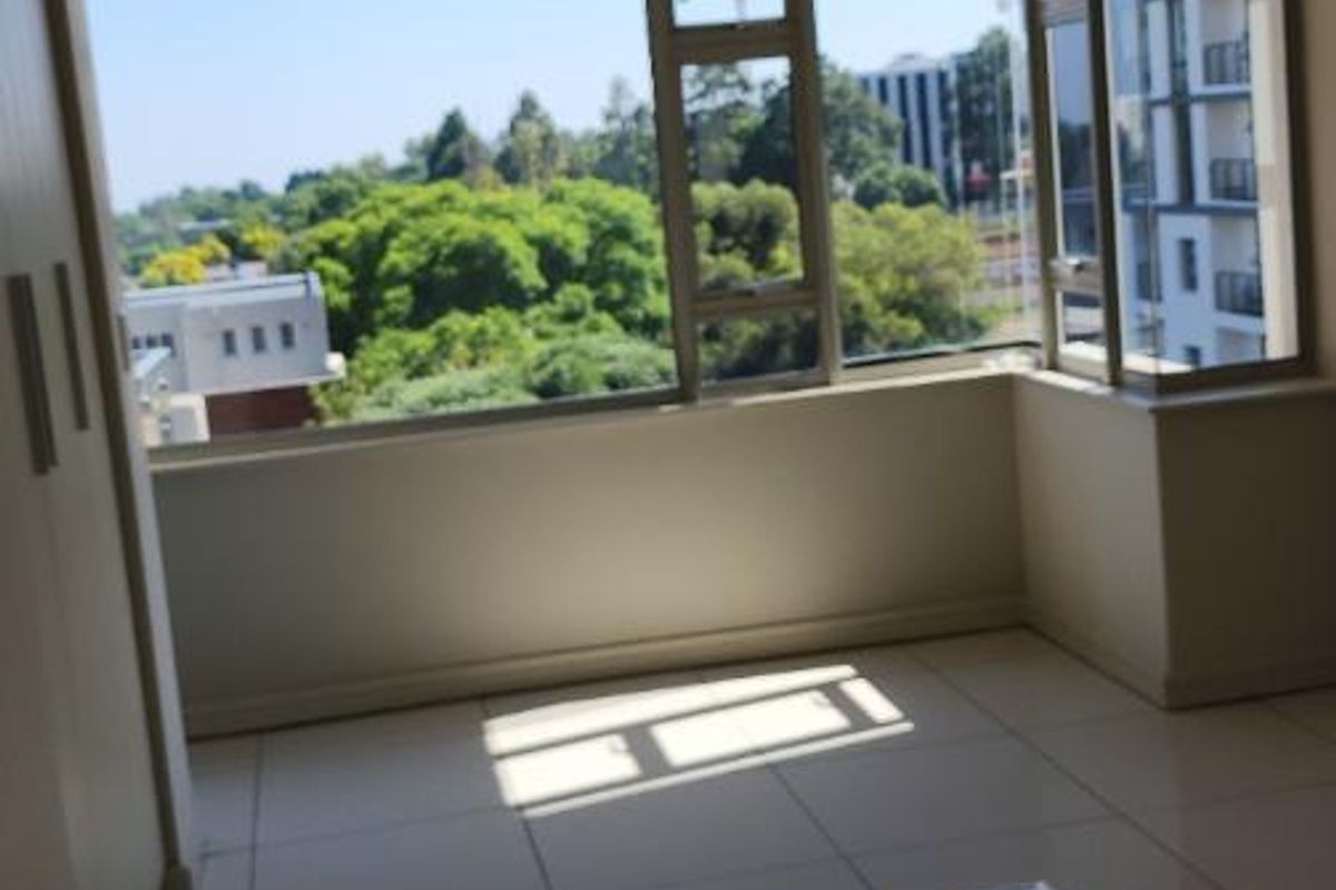 A bright, empty bedroom featuring large bay windows with expansive views, tiled flooring, and built-in cabinetry.
