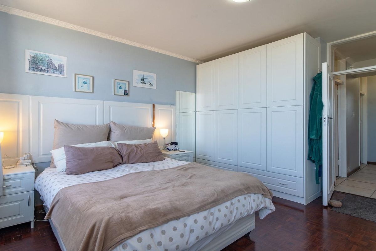 A well-maintained bedroom featuring parquet flooring, crown molding, a custom panelled headboard, and extensive built-in wardrobe storage.